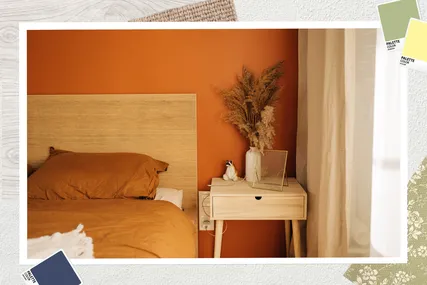 A cozy bedroom with an orange accent wall a wooden headboard a bedside table with decor items and light filtering through a curtain